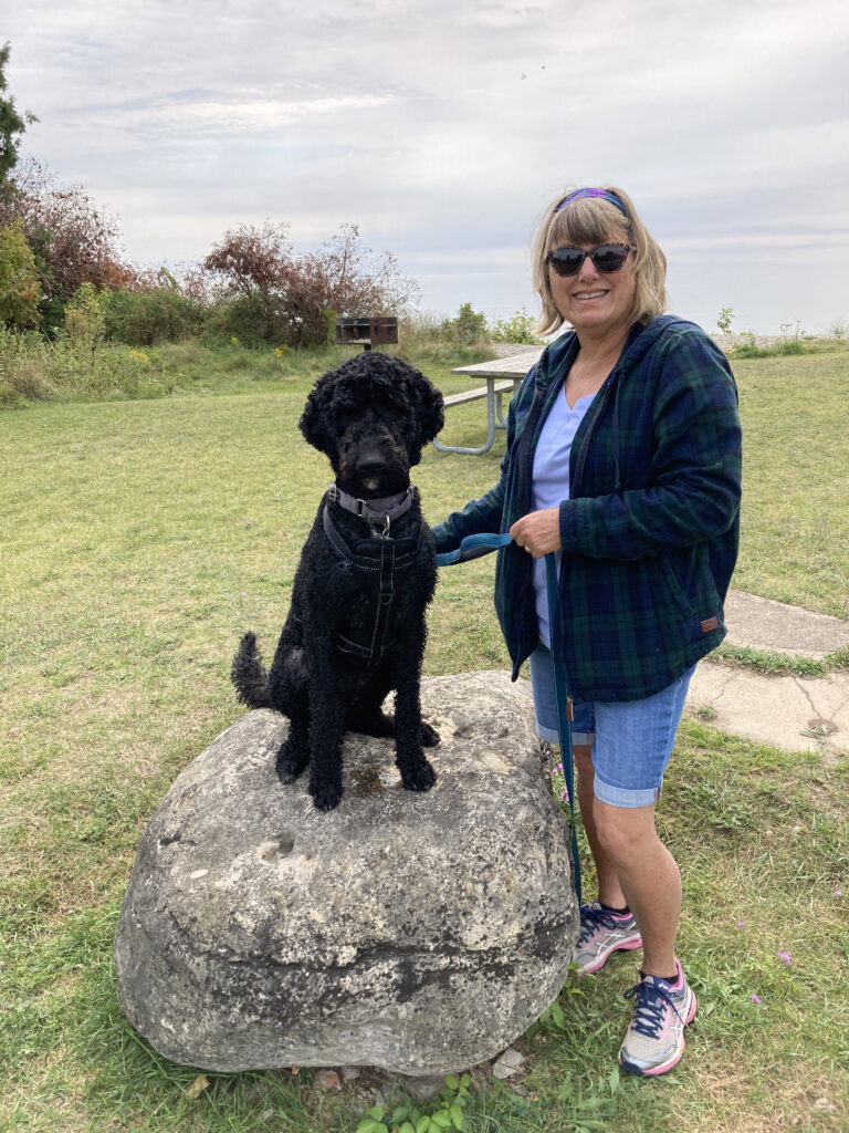 Lisa and her black goldendoodle Scout posing next to a large rock, smiling.